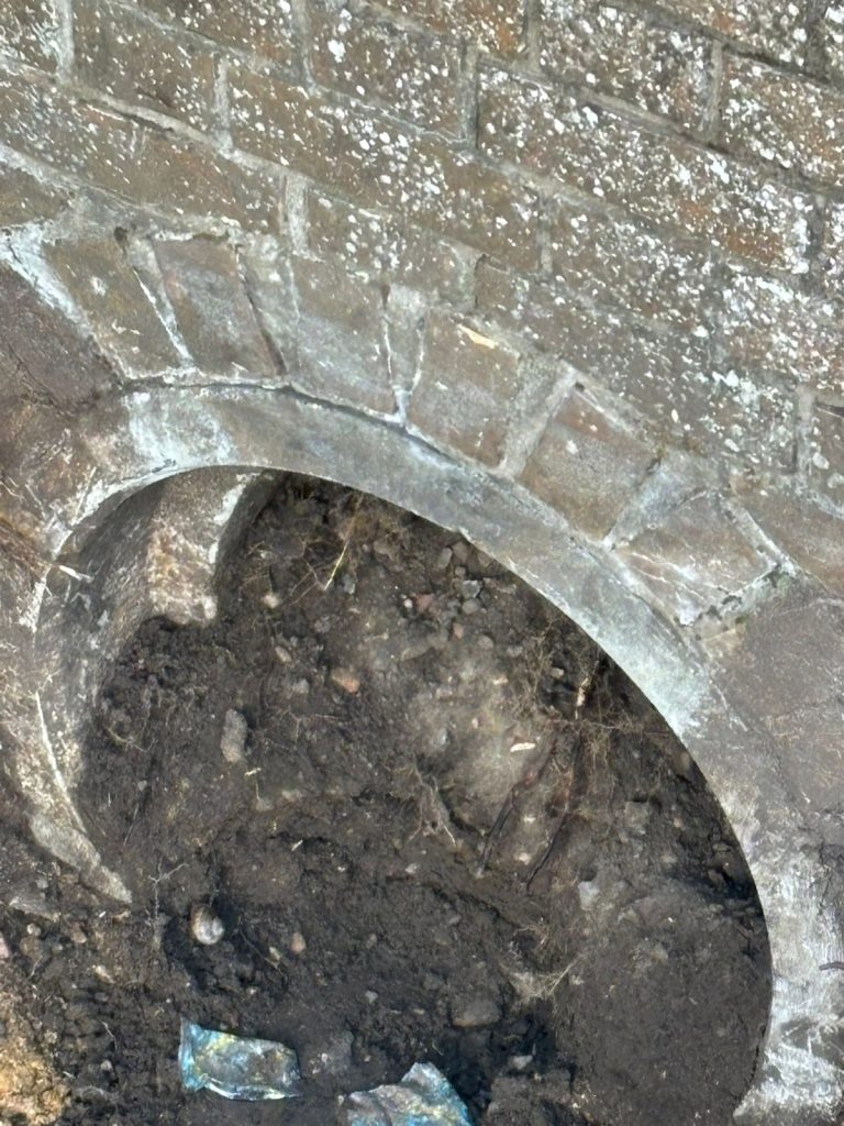 A blocked brick drainage culvert covered in mud and debris before professional cleaning