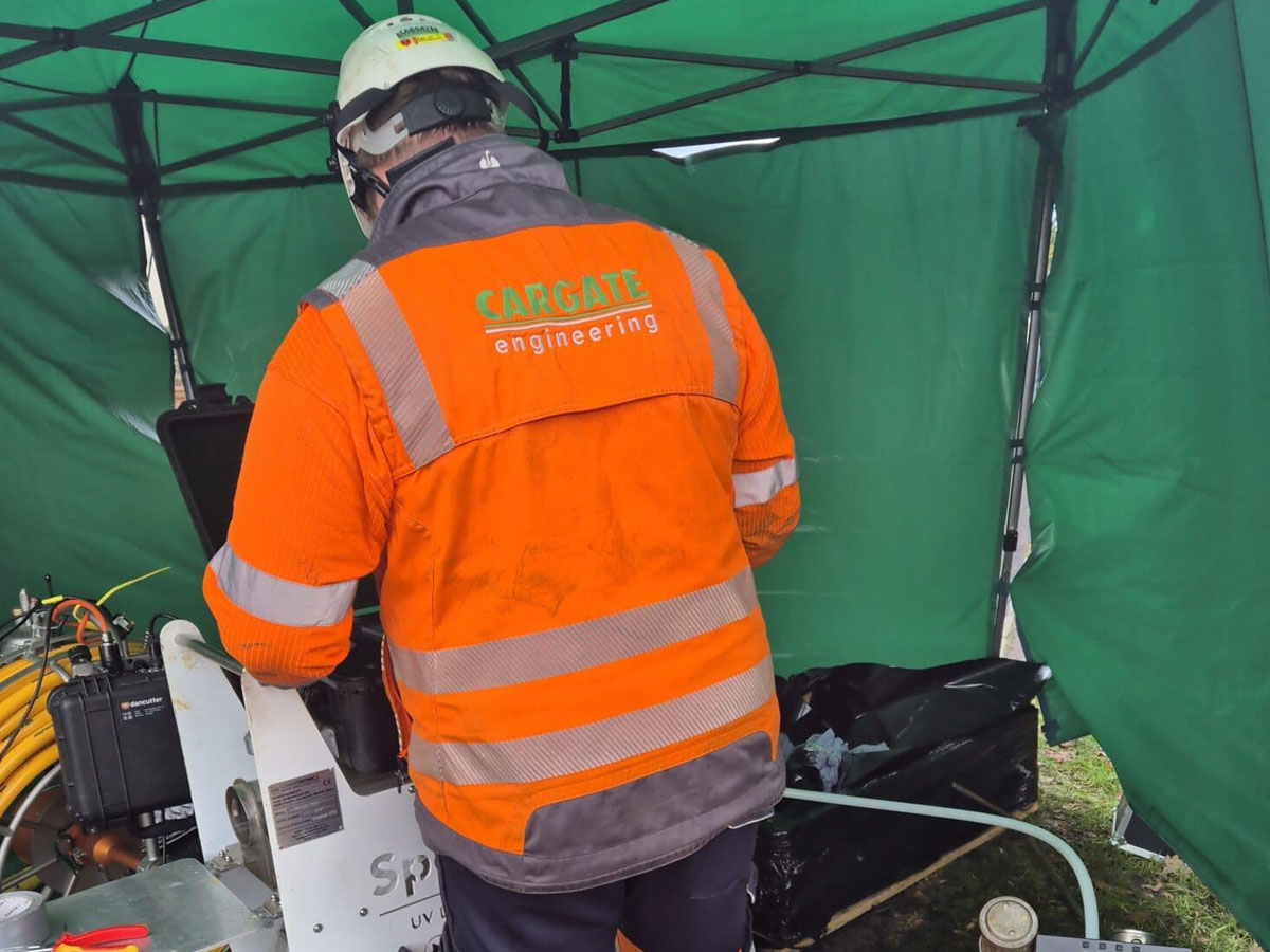 Specialist drainage engineer controlling trenchless pipe rehabilitation equipment on site.