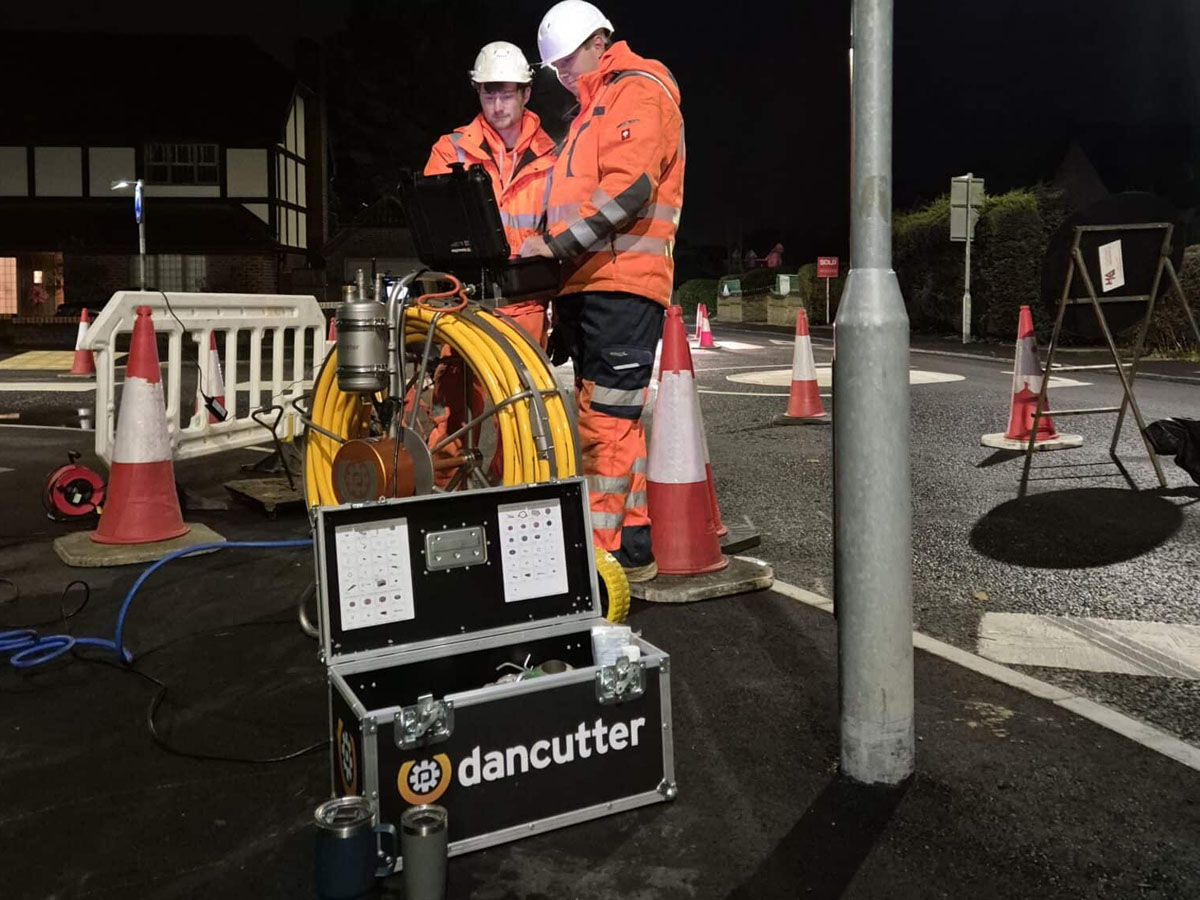 Two engineers operating Dancutter robotic equipment during night-time highway drainage works.